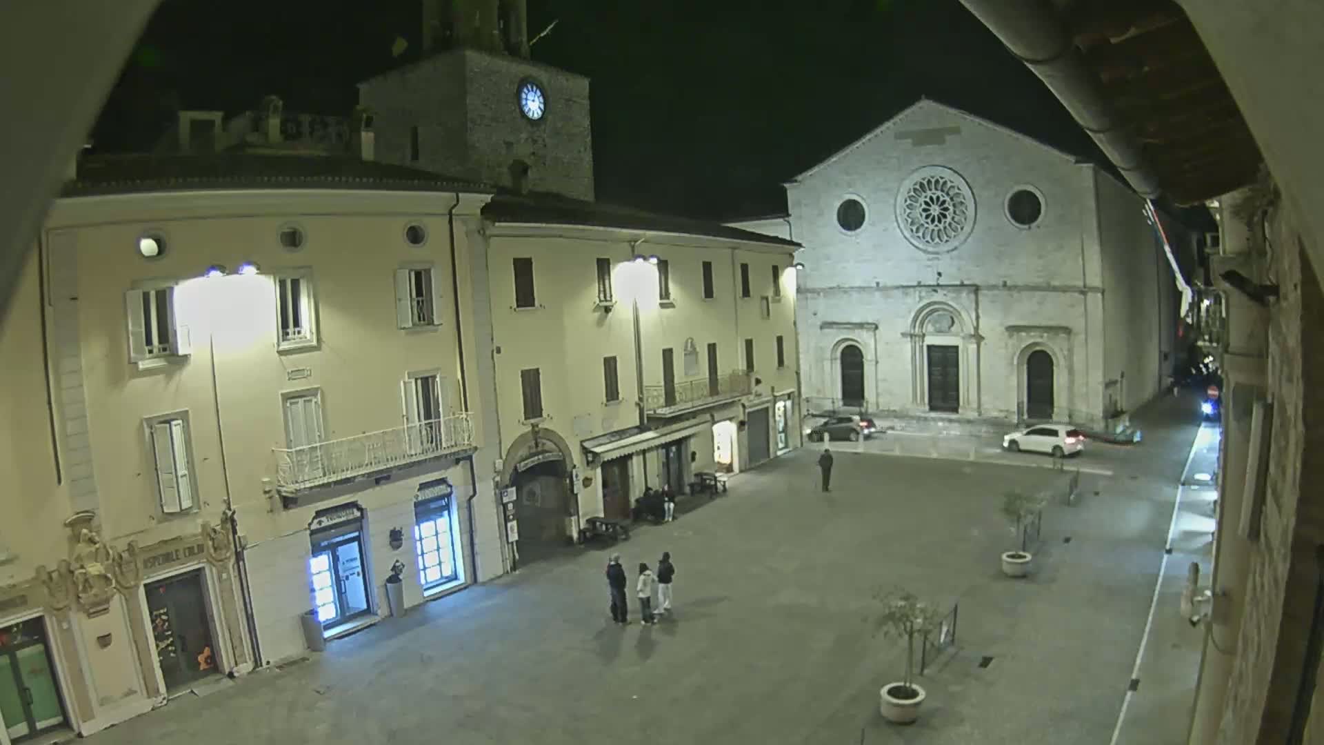 A nighttime view of a town square with several buildings, including a church with a rose window, under clear, dark skies.