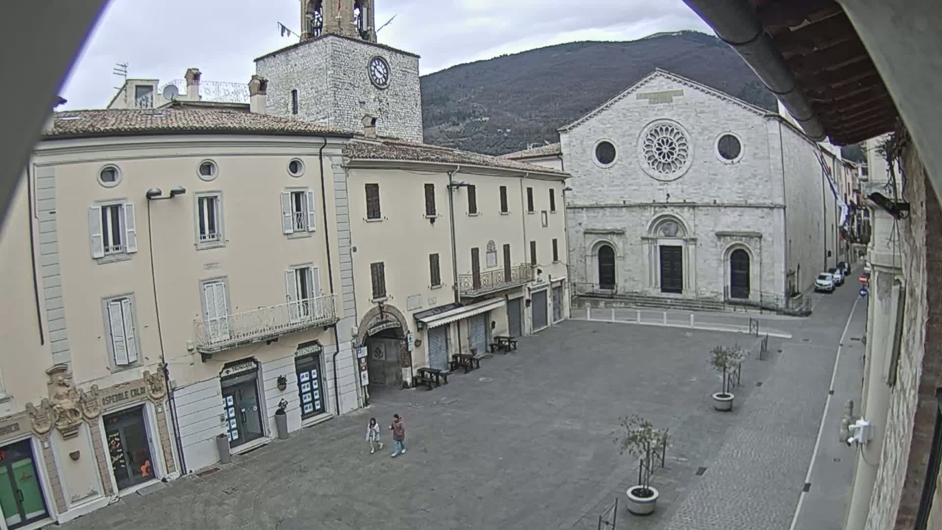 A town square with light-colored buildings, including a church with a rose window, under an overcast sky.