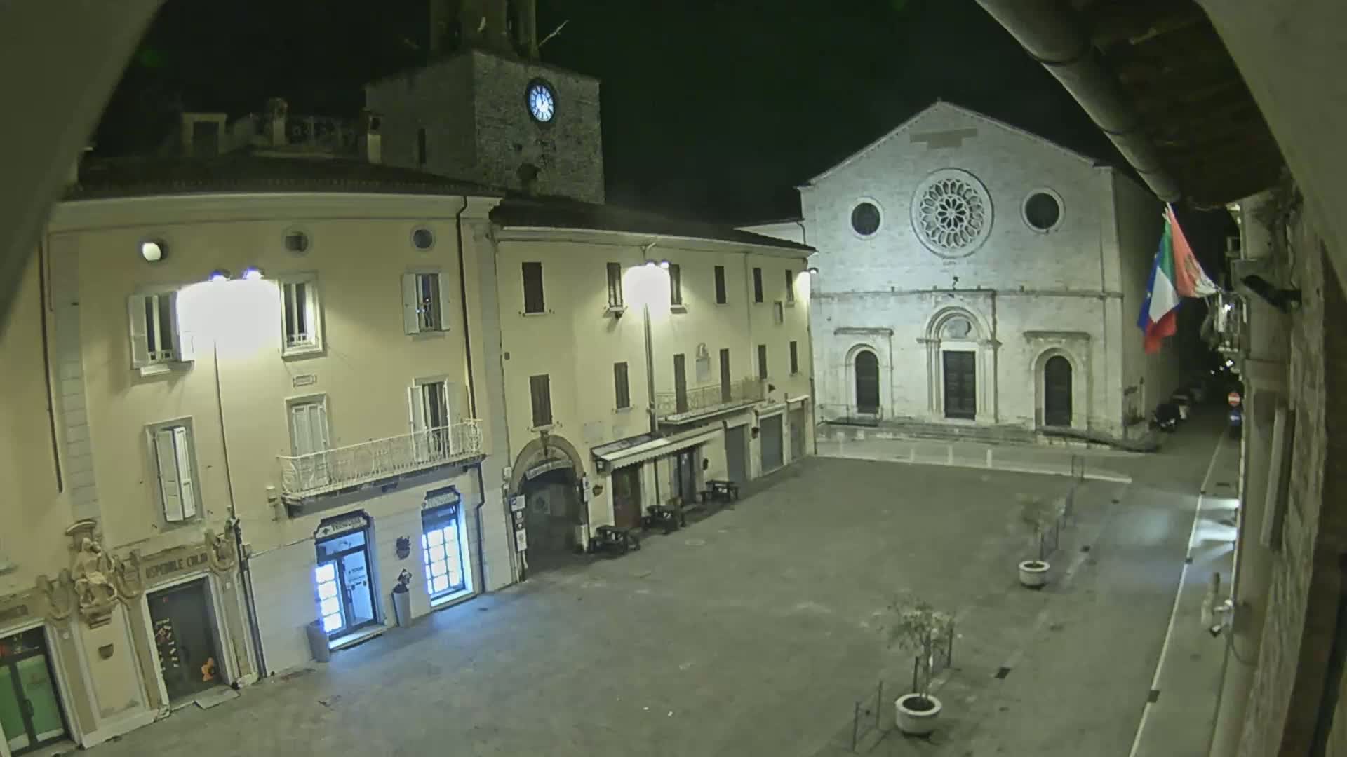 A nighttime view of a town square with buildings, including a church with a rose window, illuminated by streetlights.