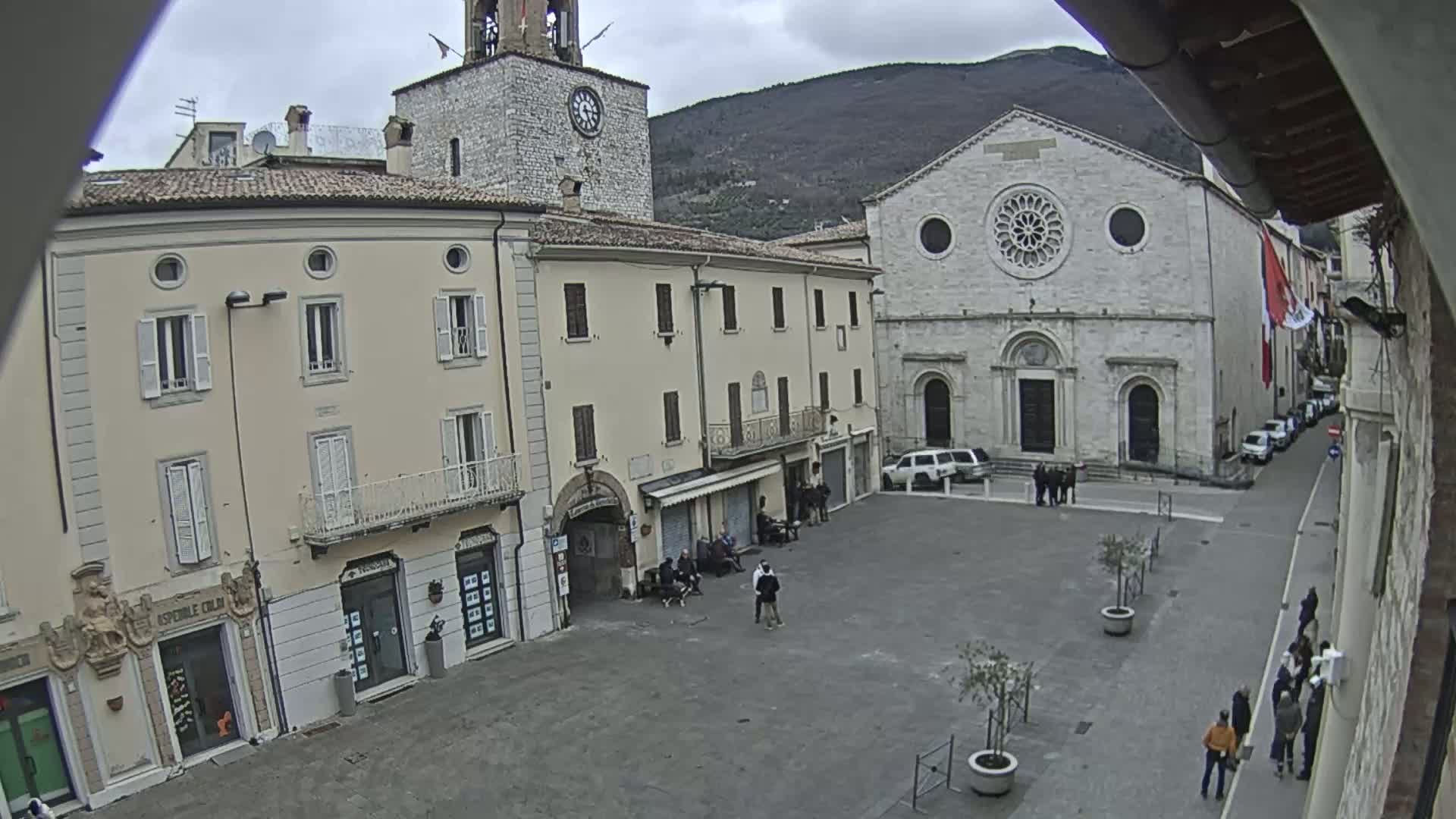 A town square with several buildings, including a church and a clock tower, is seen on an overcast day.