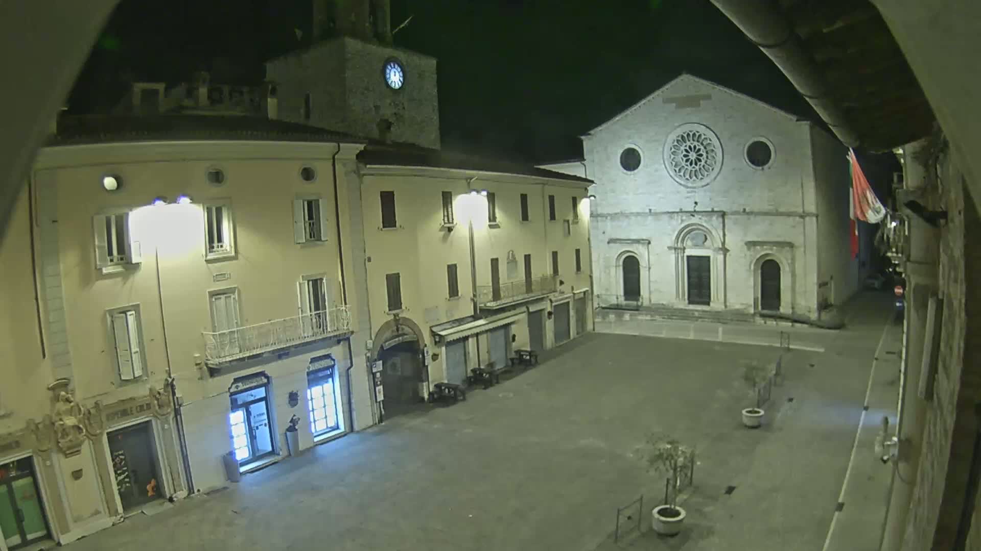 A nighttime view of a town square with several buildings, including a church with a rose window, illuminated by streetlights.