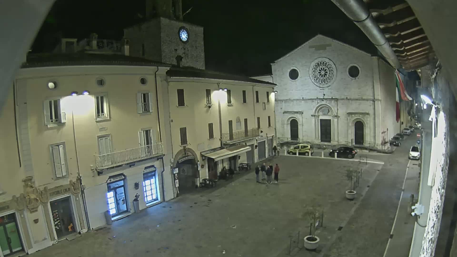 A nighttime view of a town square with several buildings, including a church with a rose window, under clear skies.
