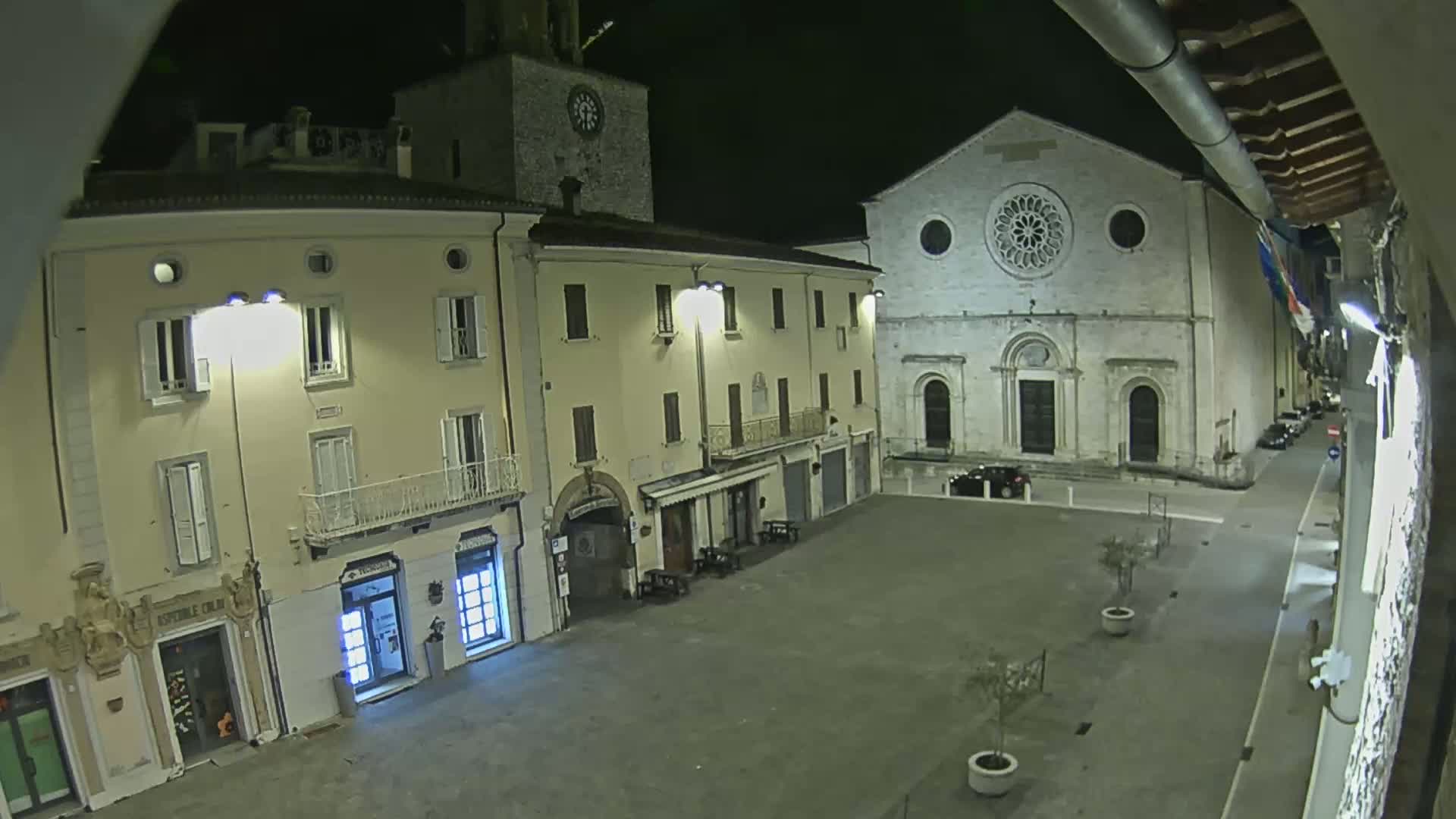 A nighttime view of a town square, featuring a large stone church and several buildings illuminated by streetlights.