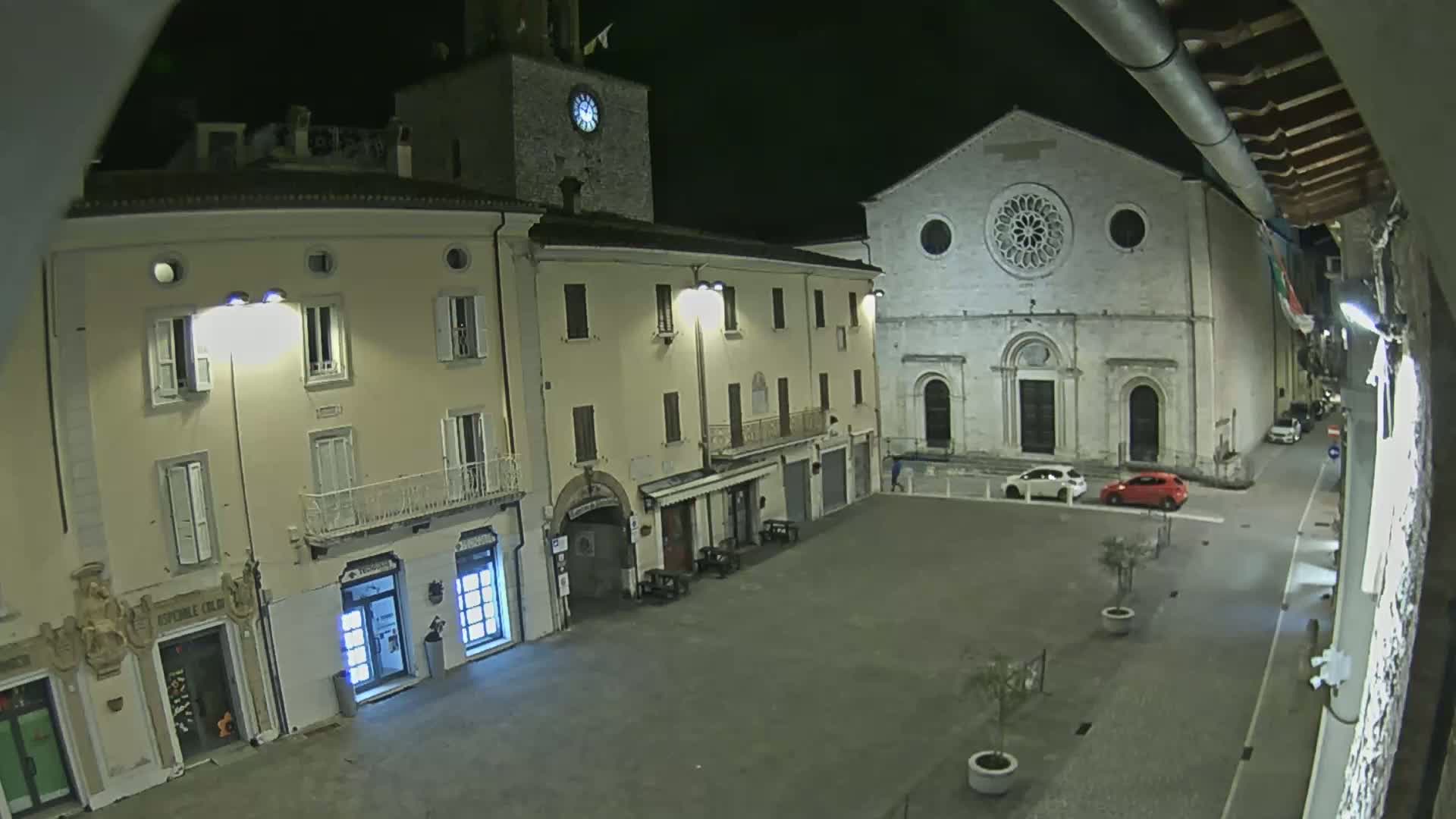 A nighttime view of a town square with several buildings, including a church with a rose window, illuminated by streetlights.