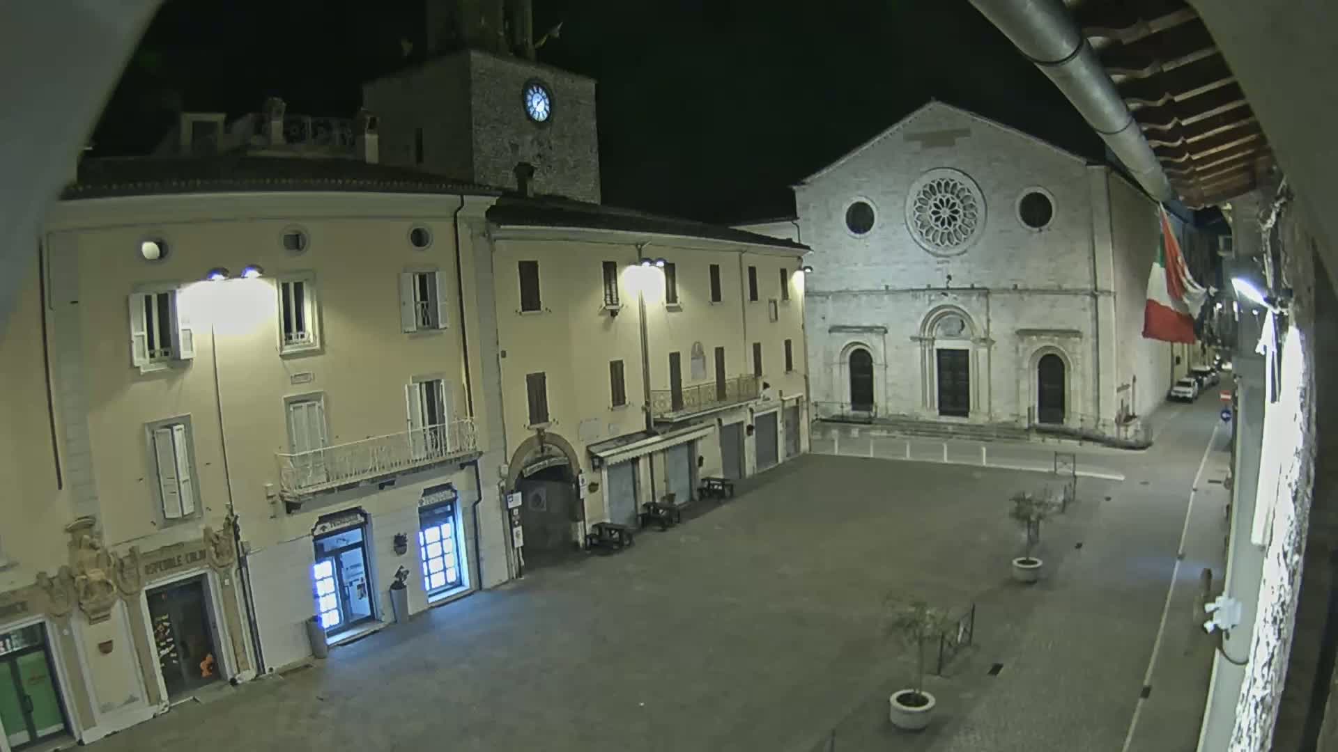 A nighttime view of a town square with several buildings, including a church with a rose window, under clear, dark skies.