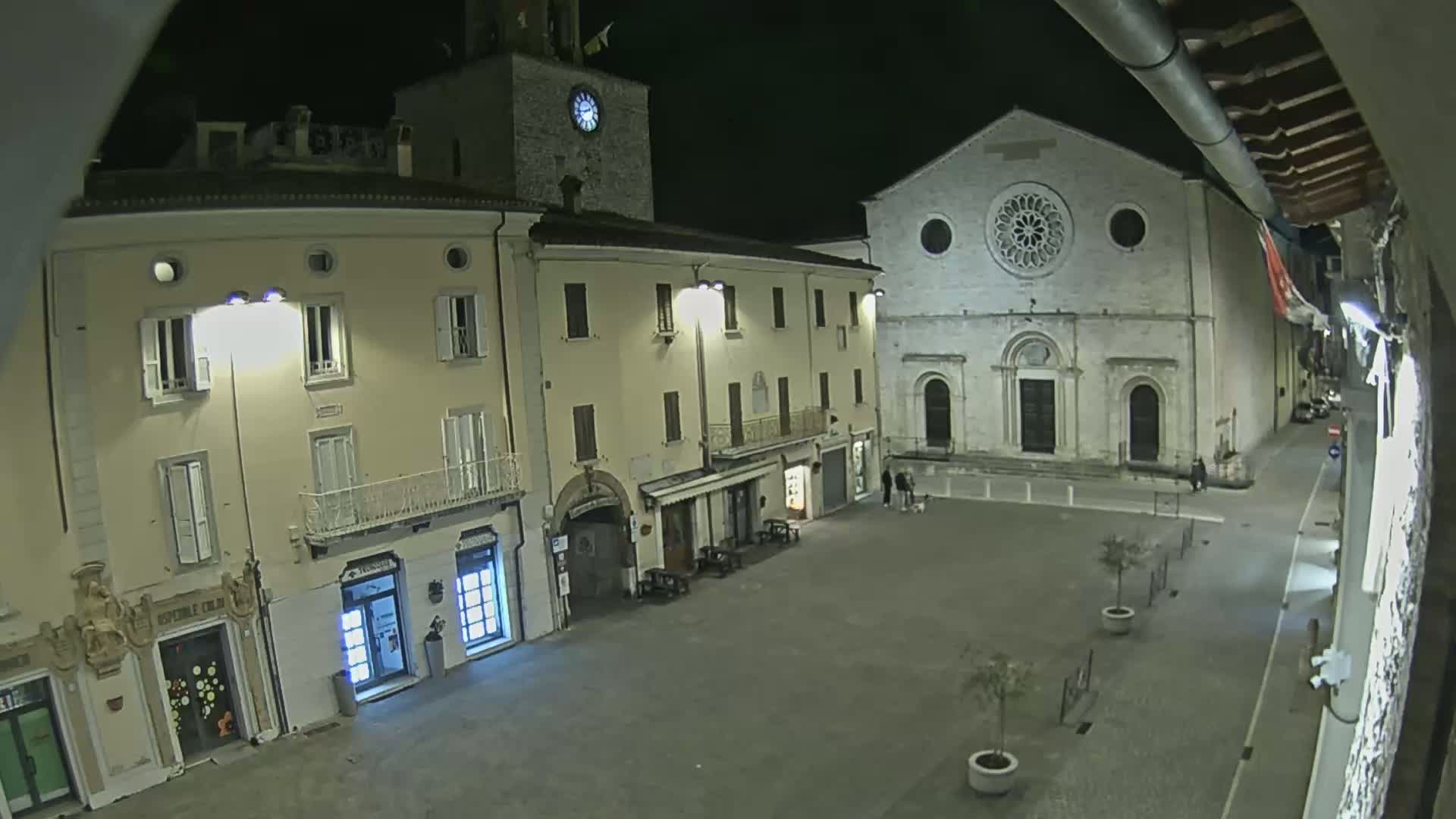 A nighttime, high-angle view of a town square, featuring several buildings including a church with a rose window, lit by streetlights.