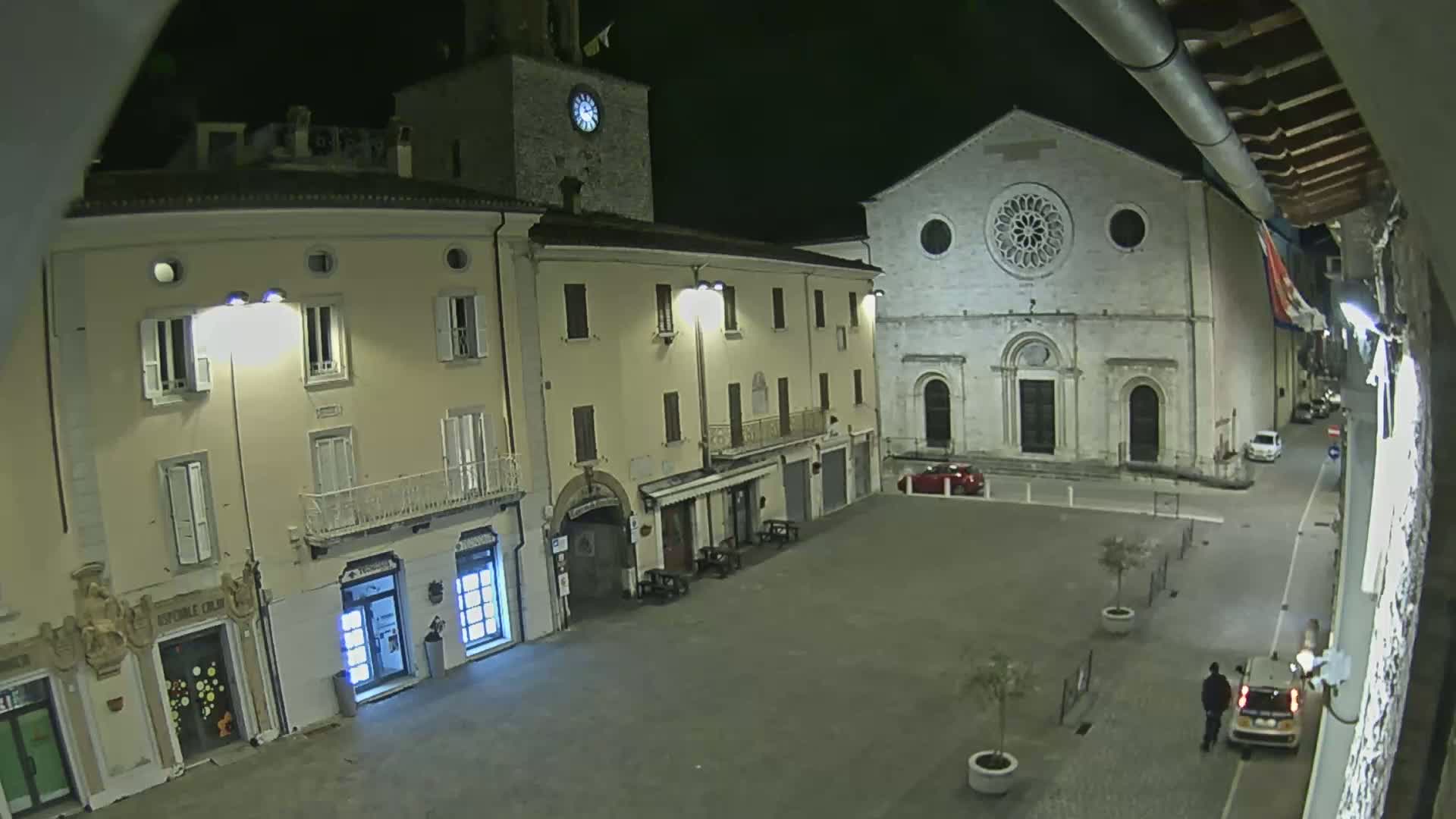 A nighttime view of a town square with buildings, including a church with a rose window, under dark, well-lit conditions.