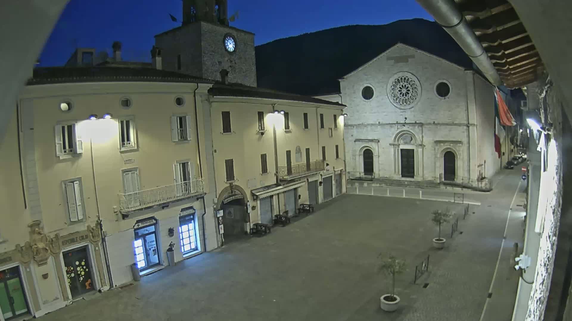 A nighttime view of a town square with several buildings, including a church with a large rose window, under a clear, dark blue sky.
