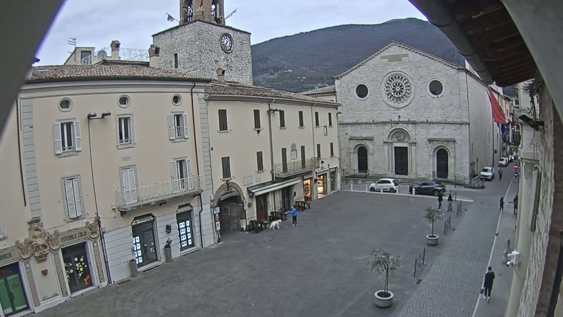 A mostly empty town square with several buildings, including a church with a rose window, under an overcast sky.