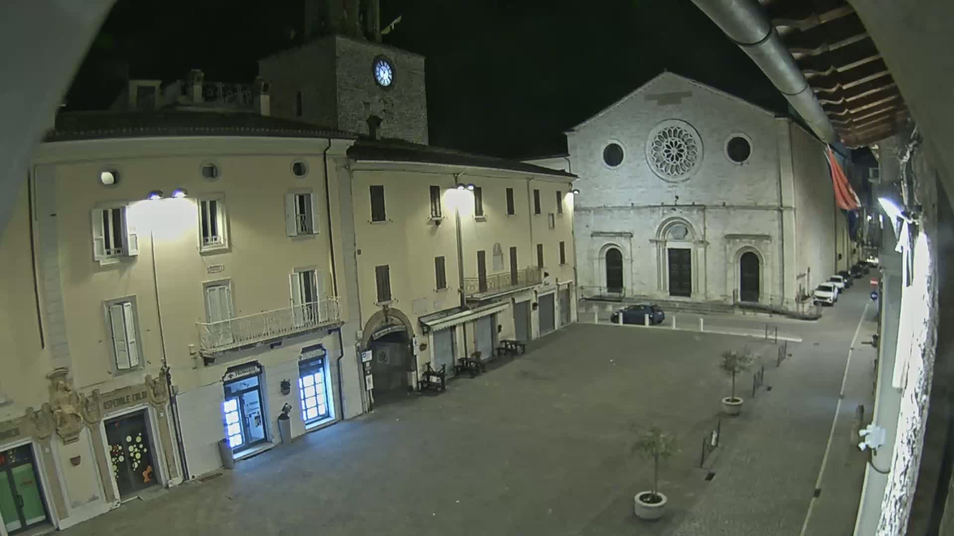 A nighttime view of a town square, featuring several buildings including a church with a rose window, lit by streetlights.