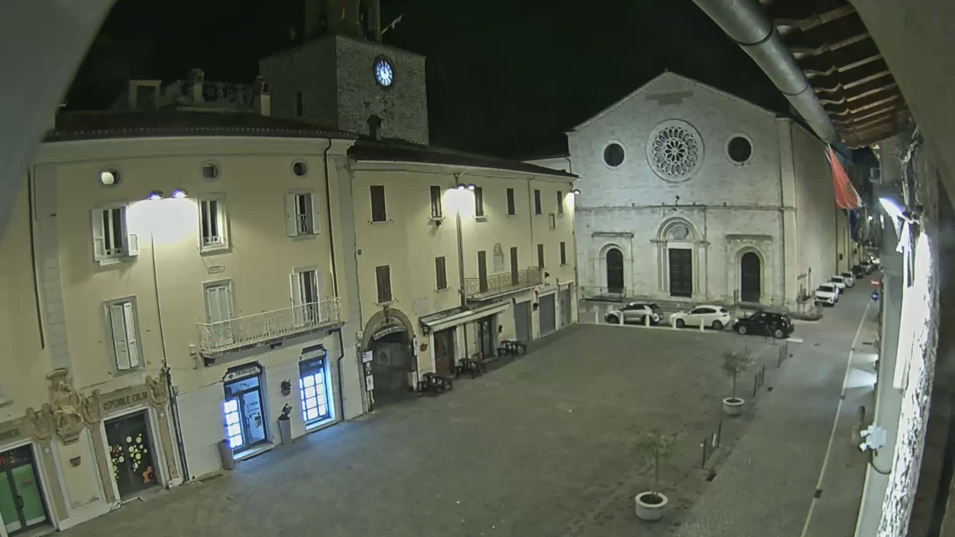 A nighttime view of a town square with several buildings, including a church with a large rose window, under clear skies.