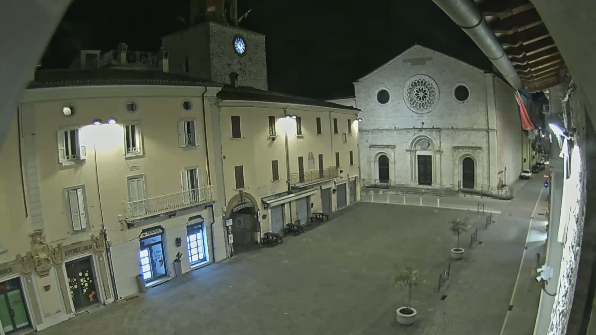 A nighttime view of a town square with several buildings, including a church with a rose window, under clear skies.