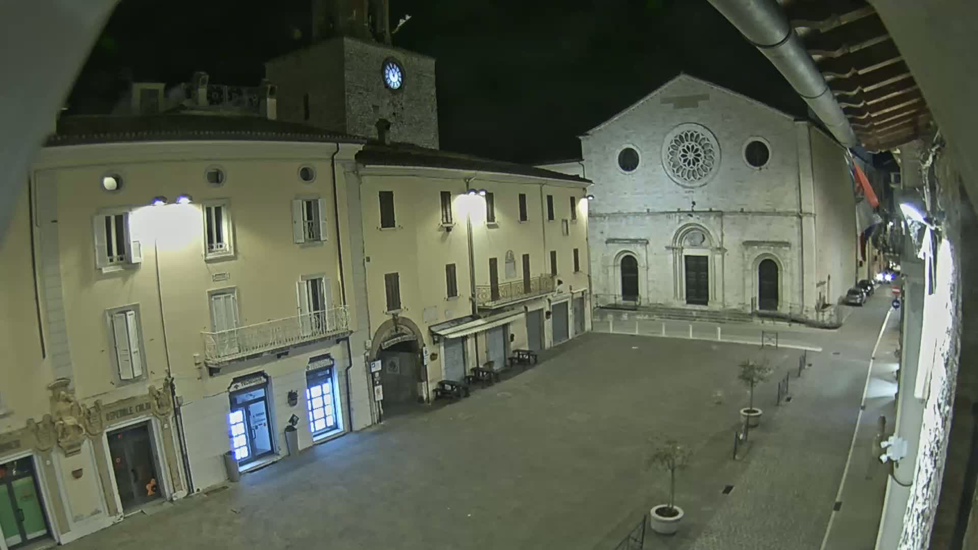 A nighttime, high-angle view of a town square with several buildings, including a church with a rose window, under artificial light.