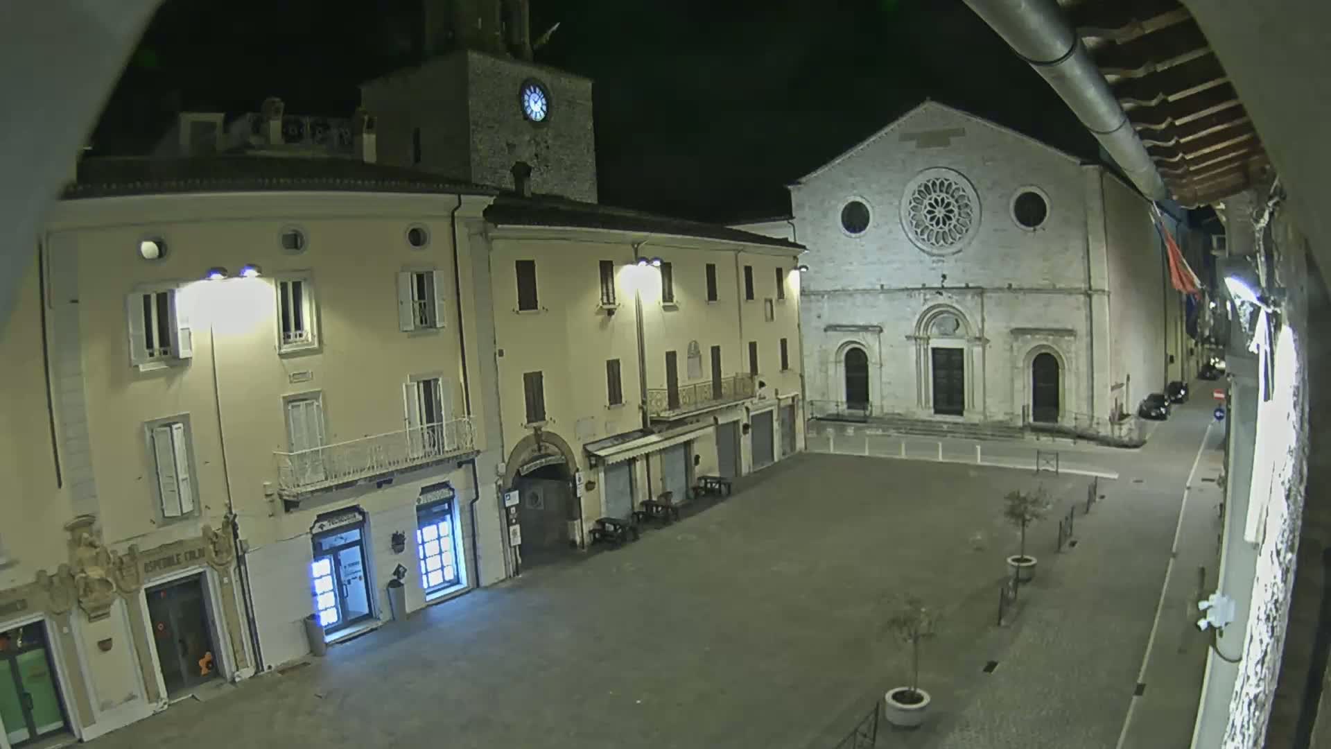 A nighttime view of a town square with buildings, including a church with a rose window, illuminated under a dark sky.
