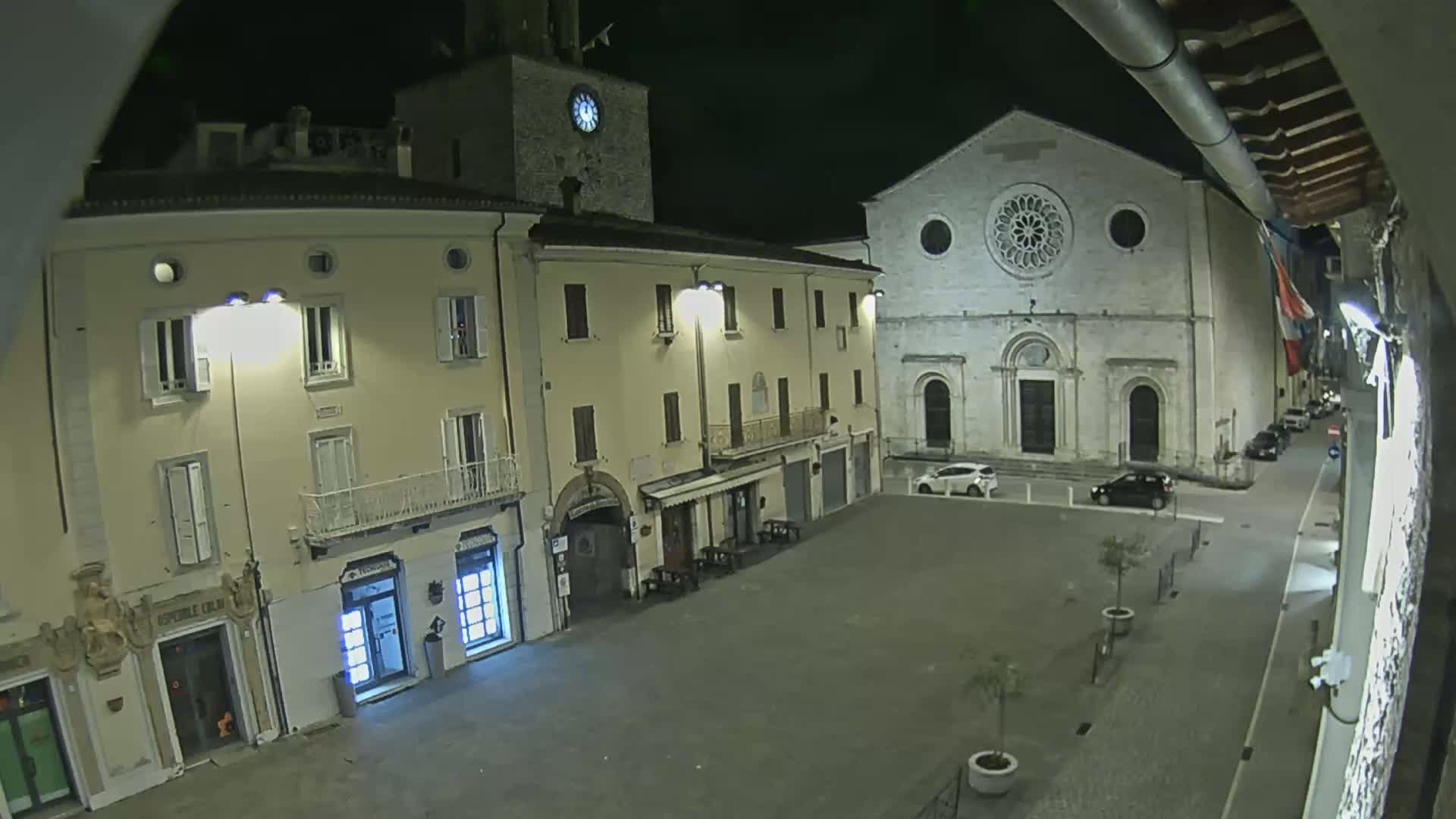 A nighttime view of a town square with several buildings, including a church with a large rose window, under a clear, dark sky.