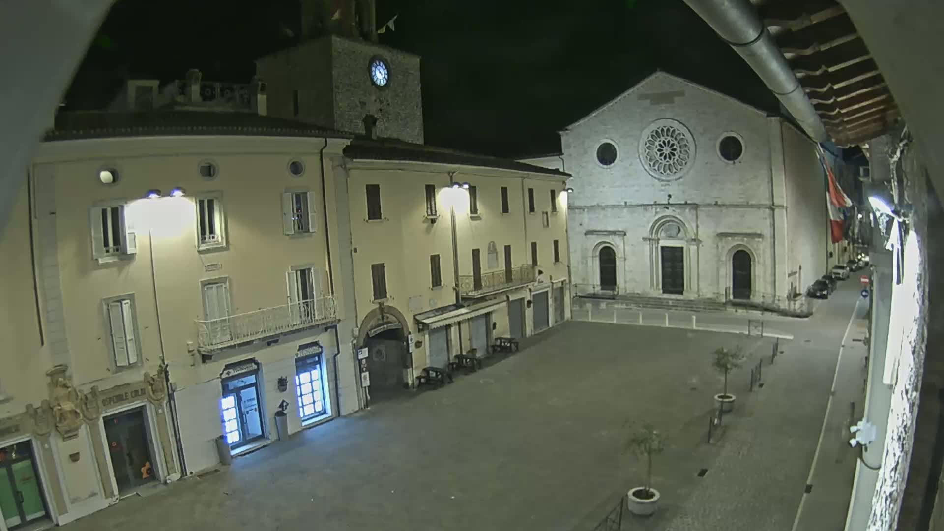 A nighttime view of a town square with several buildings, including a church with a rose window, under clear skies.