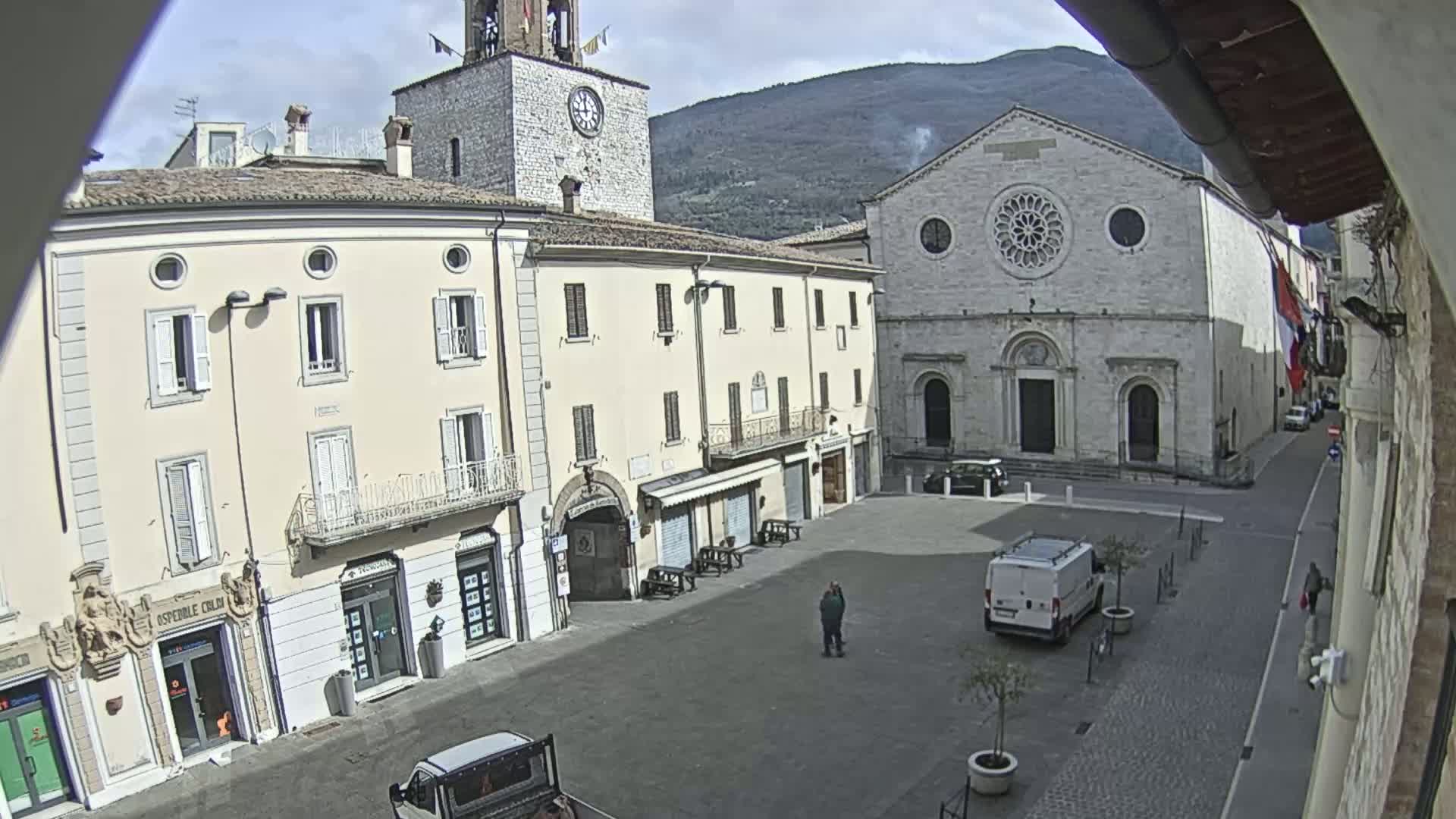 A mostly empty town square is shown on an overcast day, with several light-colored buildings, including a church with a rose window, surrounding it.