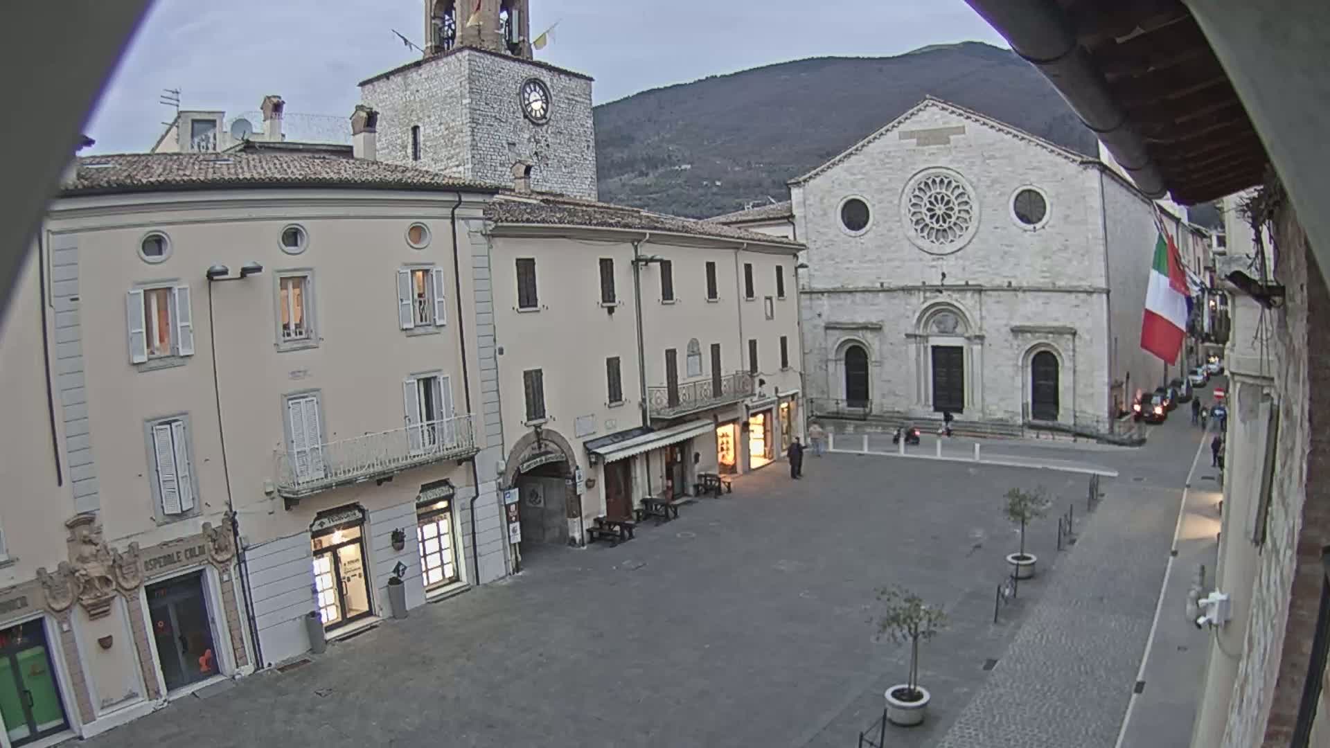 A town square with light-colored buildings, including a church with a large rose window, under an overcast sky.