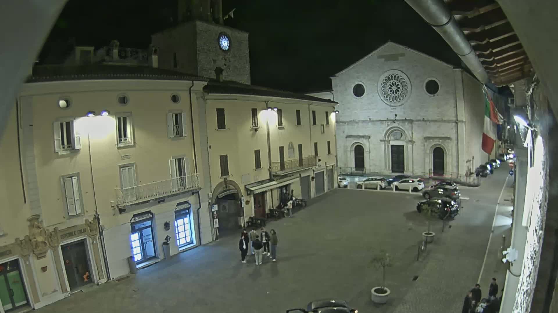 A nighttime view of a town square with several buildings, including a church with a rose window, illuminated by streetlights.