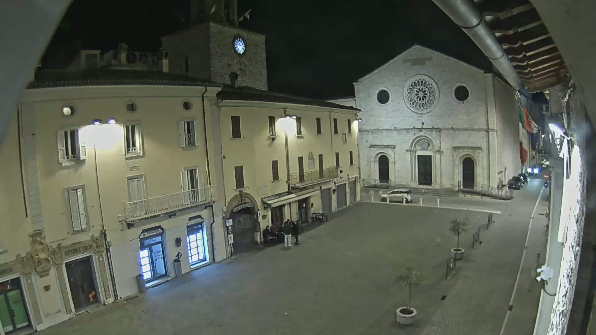 A nighttime view of a town square with several buildings, including a church with a rose window, under clear, dark skies.