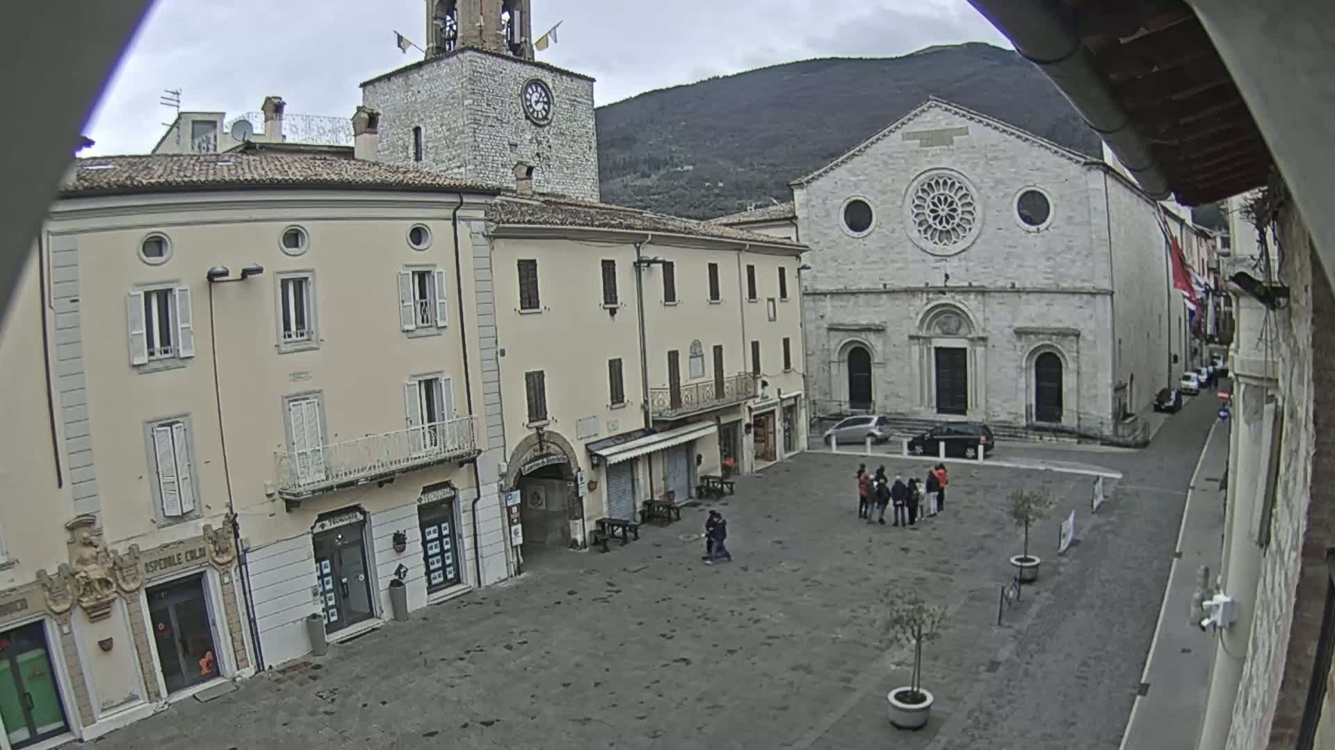 A town square with several buildings, including a church with a rose window, under an overcast sky.