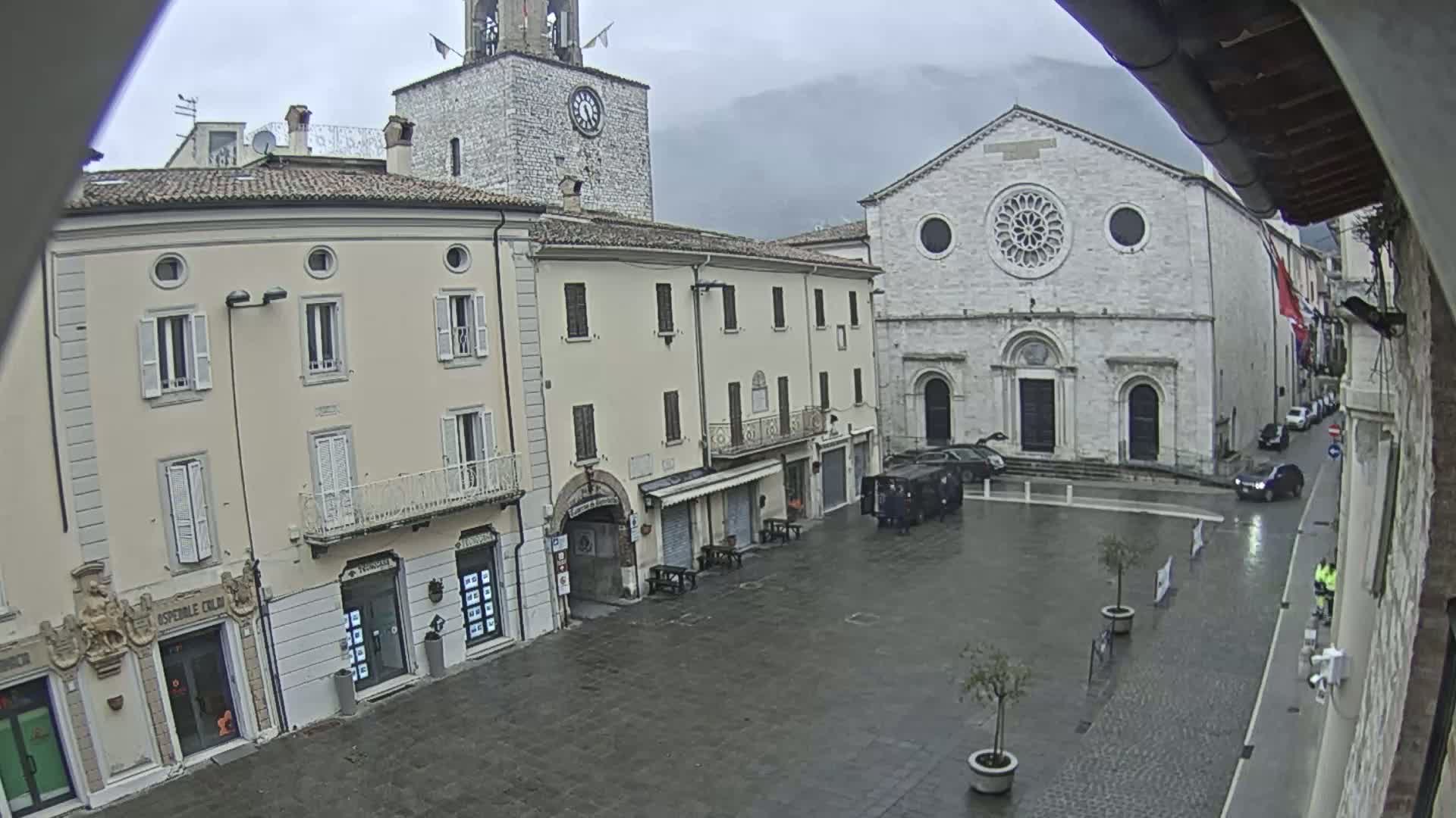 A town square with several buildings, including a church with a large rose window, under an overcast sky.
