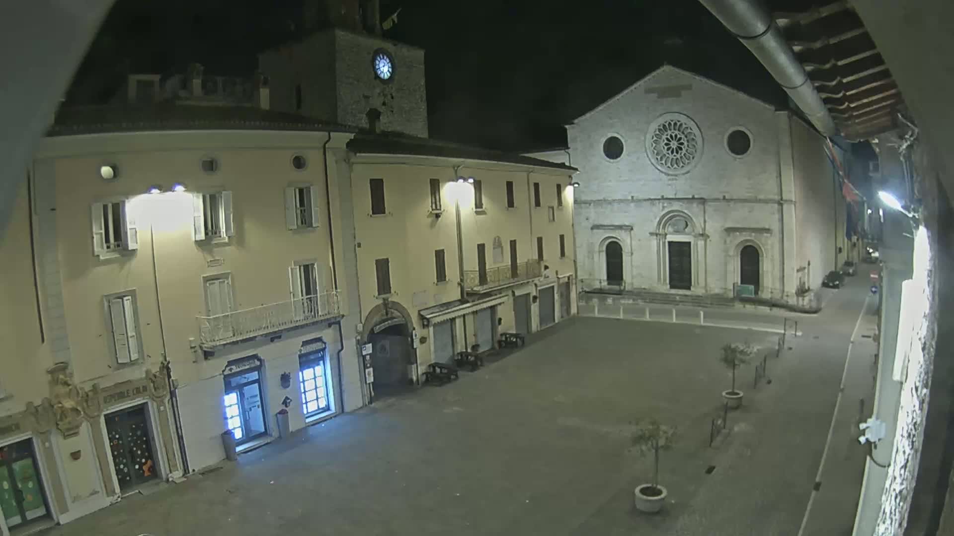 A nighttime view of a town square with buildings, including a church with a rose window, lit by streetlights.