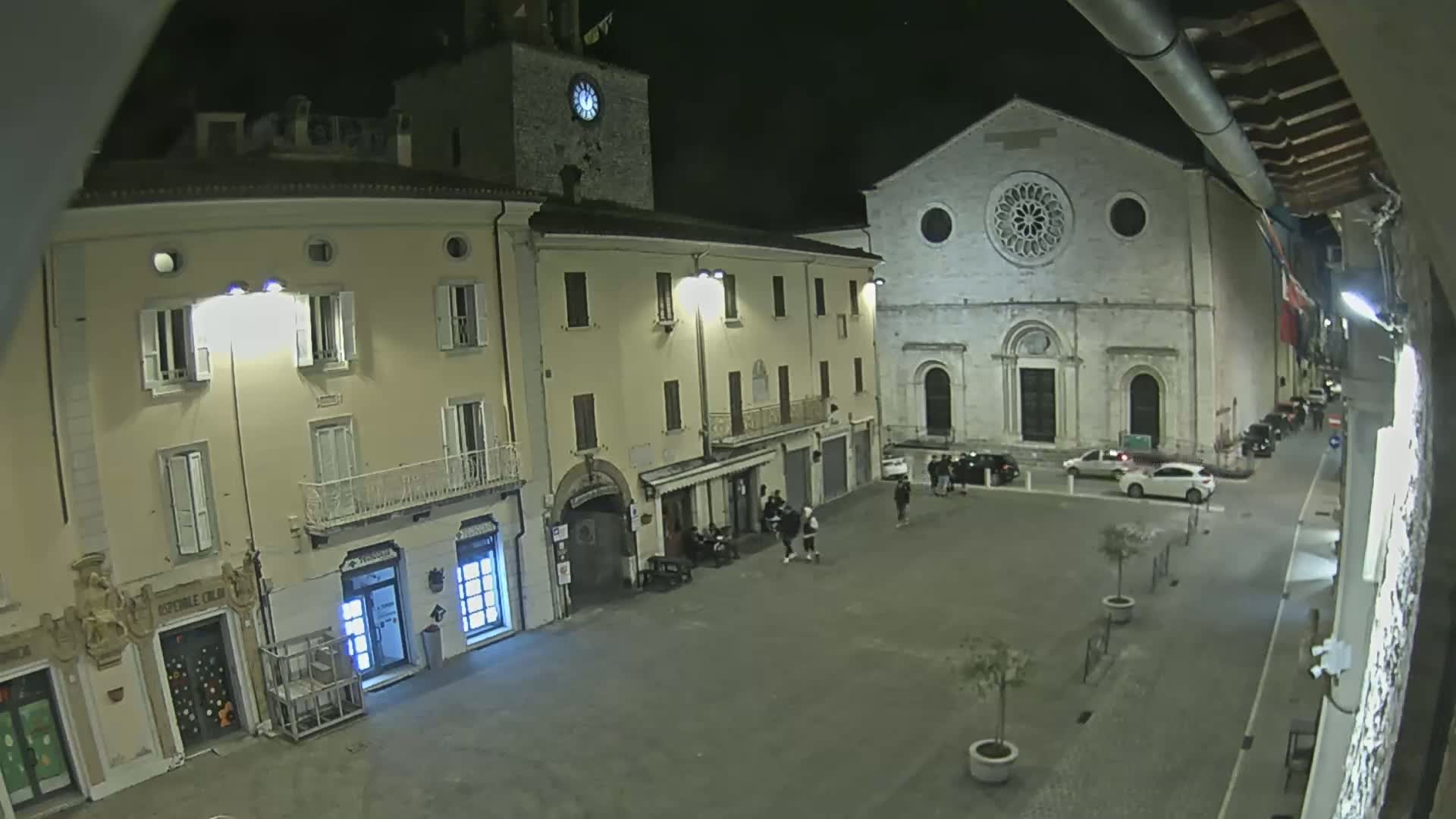A nighttime view of a town square with several buildings, including a church with a rose window, under dark, clear skies.