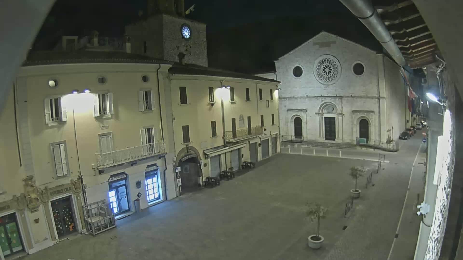A nighttime view of a town square shows several buildings, including a church with a rose window, under dark, clear skies.