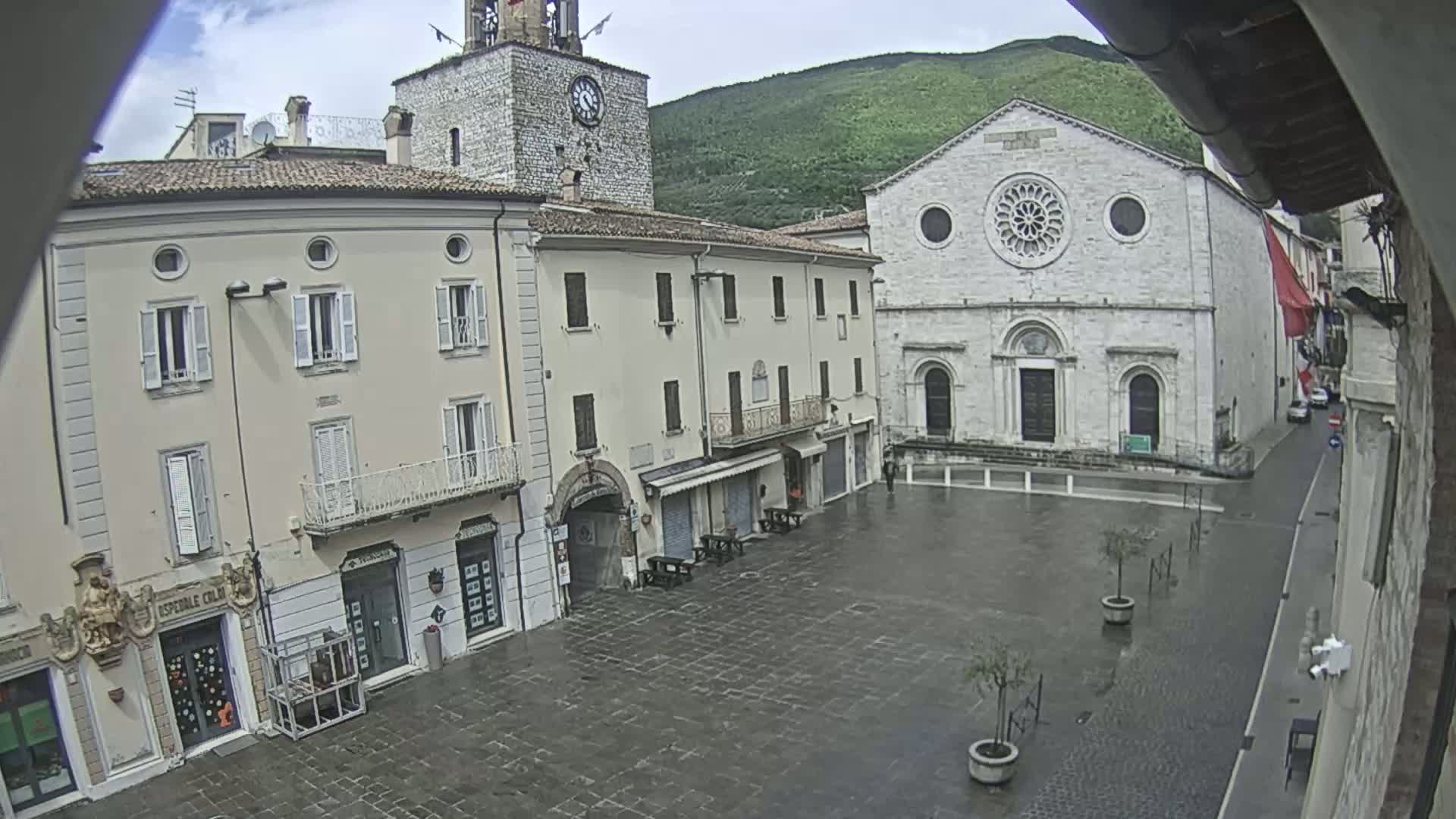A town square with several buildings, including a clock tower and a large church, is seen on a wet, overcast day.