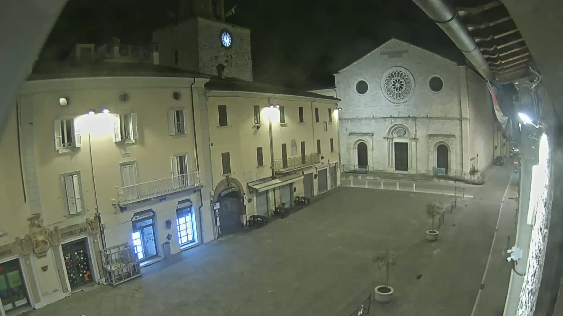 A nighttime view of a town square with several buildings, including a church with a large rose window, illuminated by streetlights.