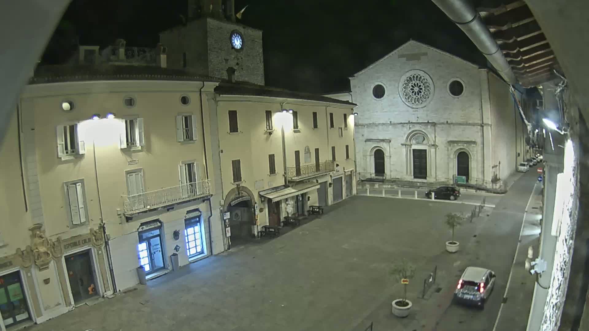 A nighttime view of a mostly empty town square, featuring a large stone church and several buildings illuminated by streetlights.