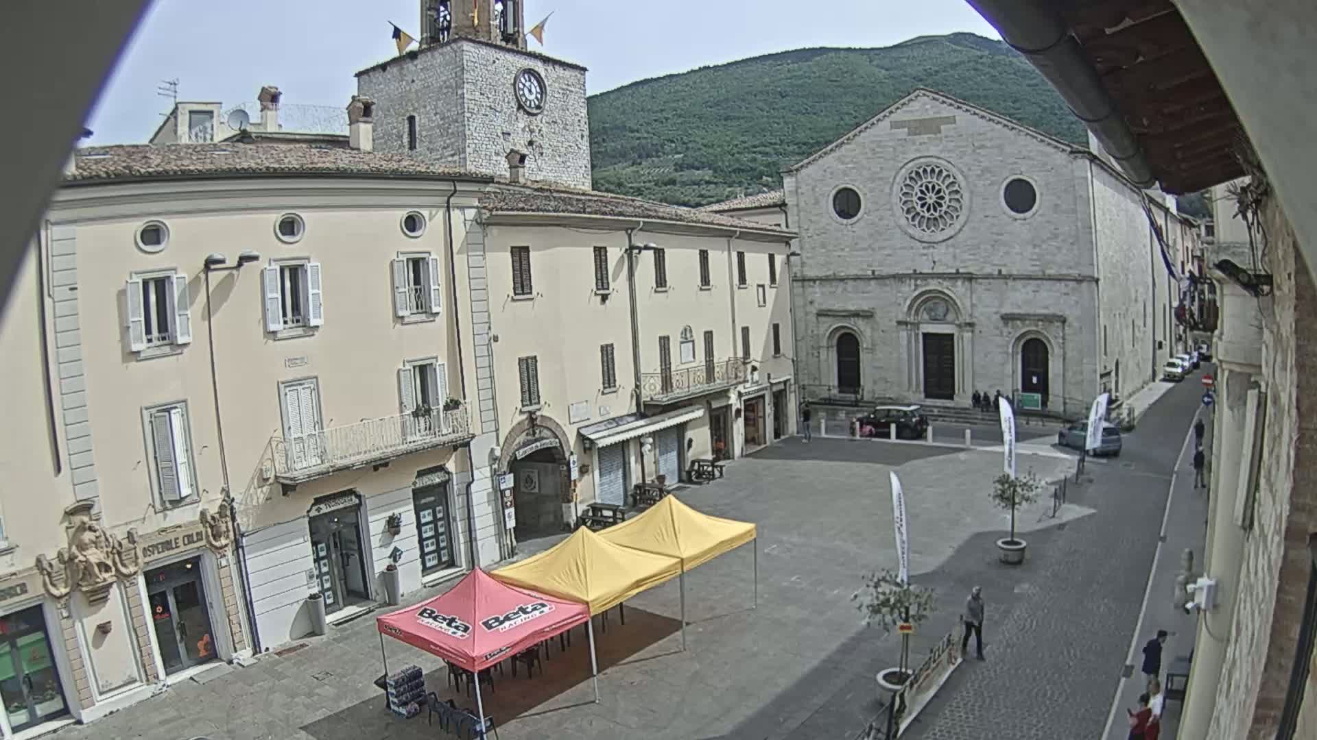 A town square with several buildings, including a church with a rose window, under a mostly sunny sky.