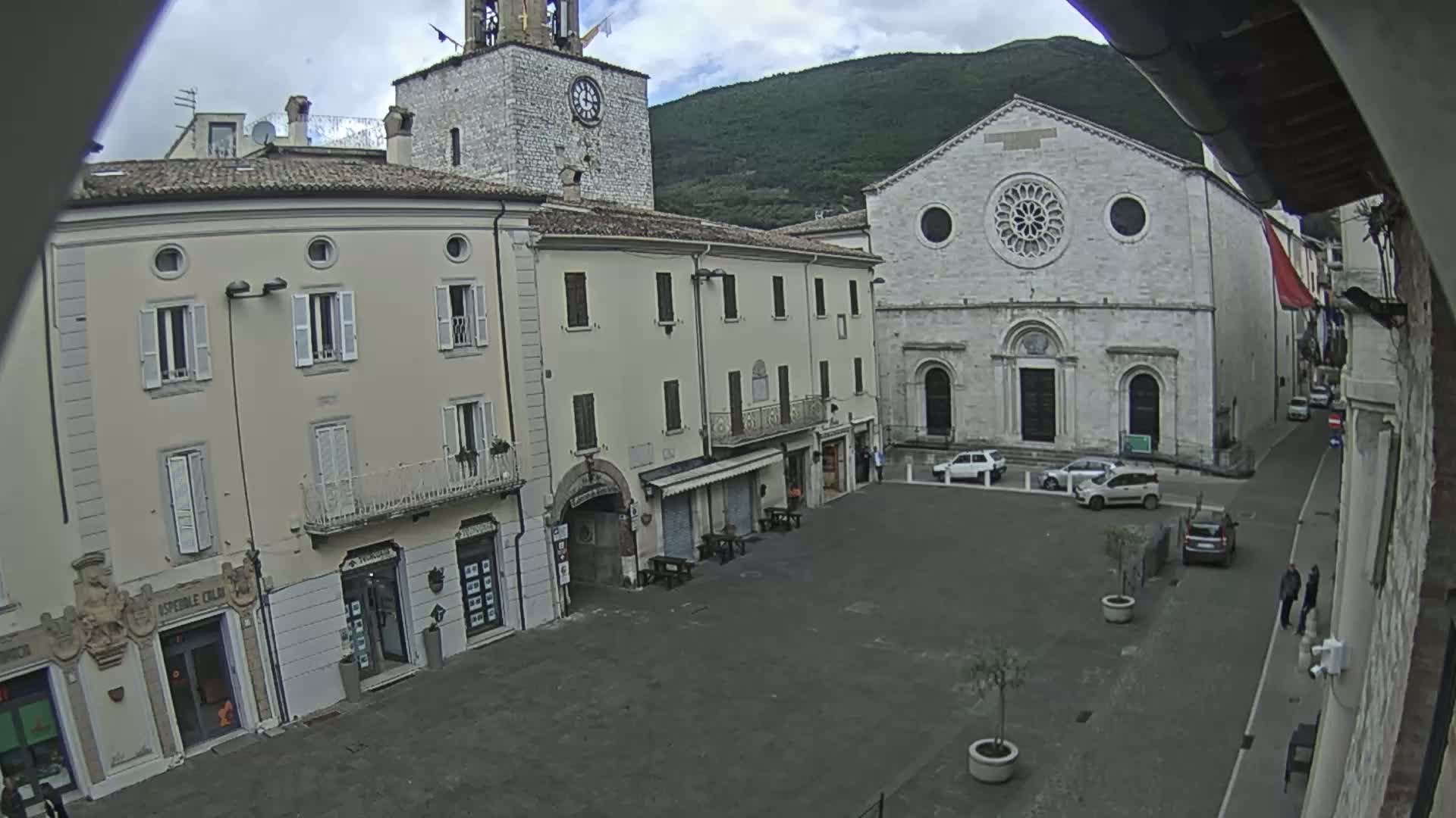 A town square with several buildings, including a church with a rose window, under overcast skies.