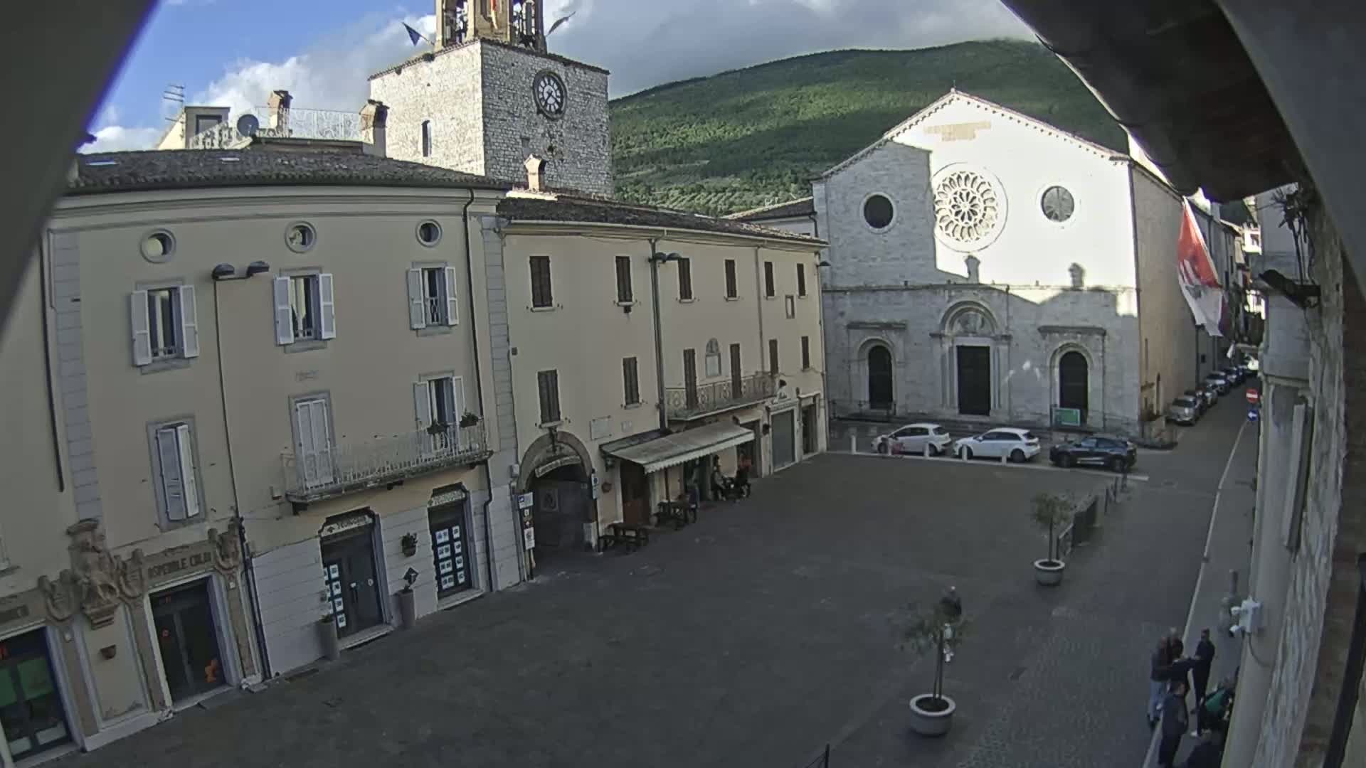 A town square with several buildings, including a church with a rose window, under overcast skies.