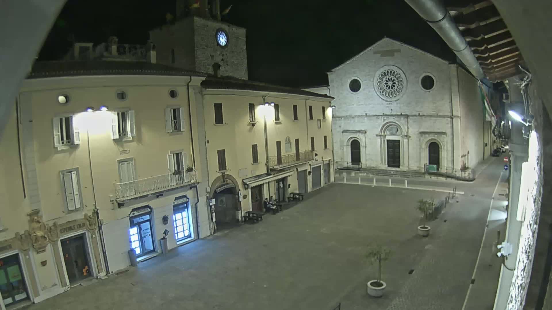A nighttime view of a town square with buildings, including a church with a large rose window, under dark, clear skies.
