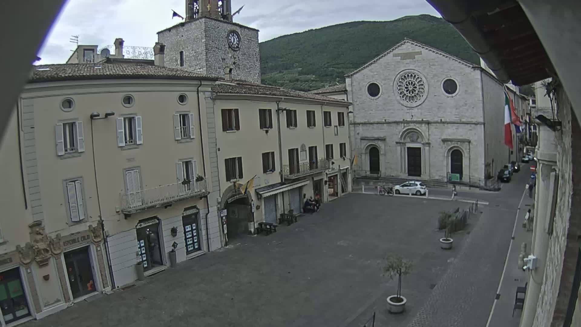 A town square with several buildings, including a church with a rose window, under an overcast sky.