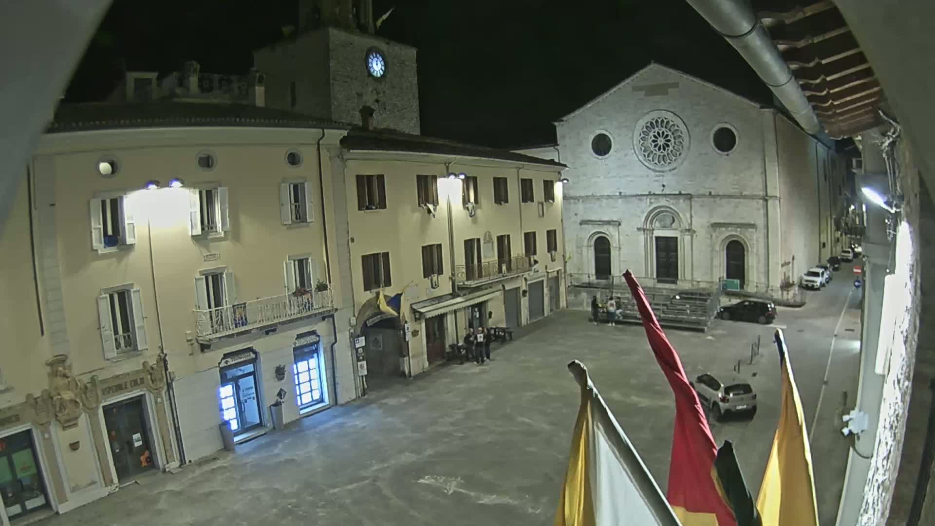 A nighttime view of a town square with several buildings, including a church with a rose window, under a clear sky.