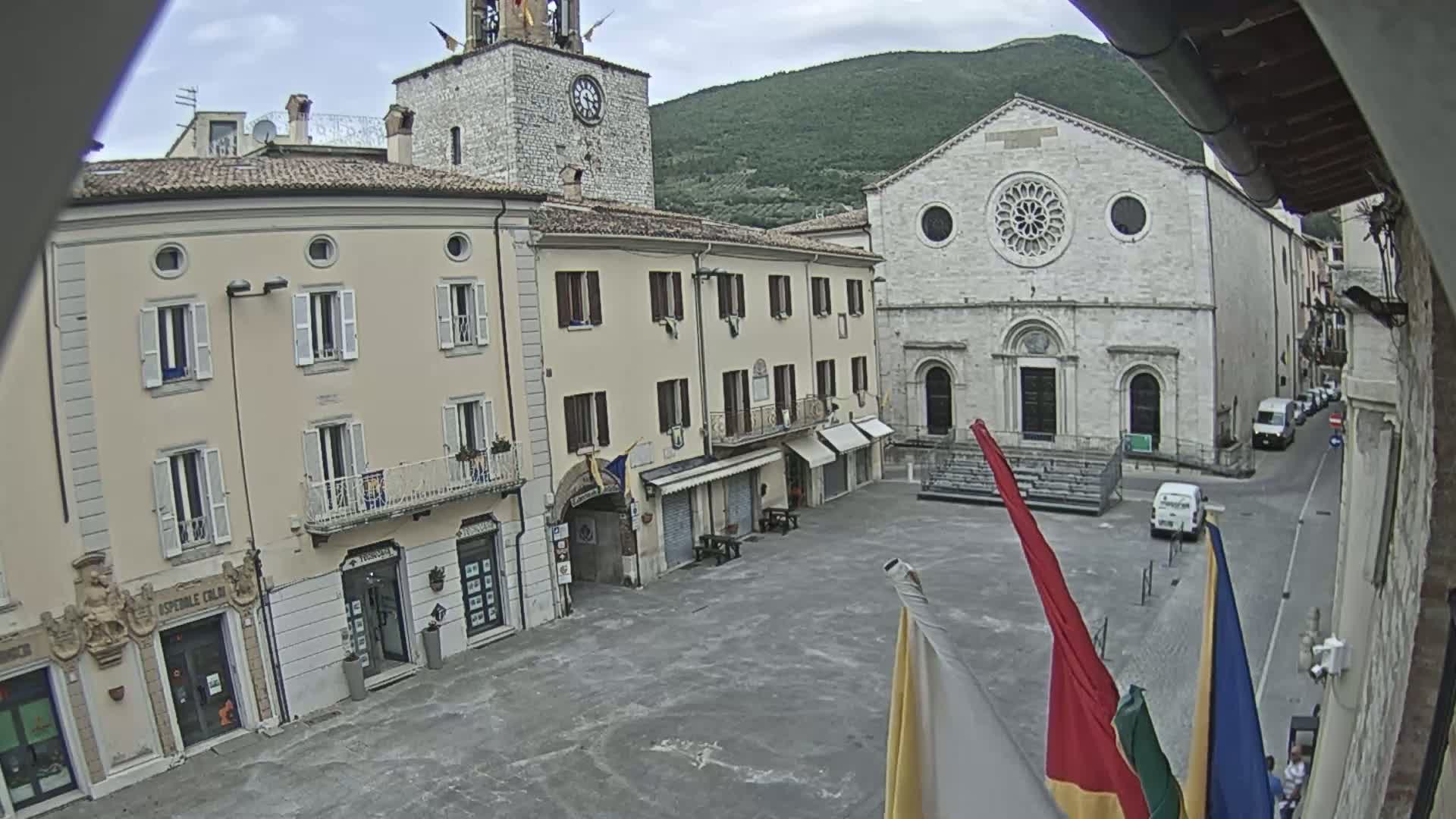 A town square with several buildings, including a church with a rose window, under a cloudy sky.