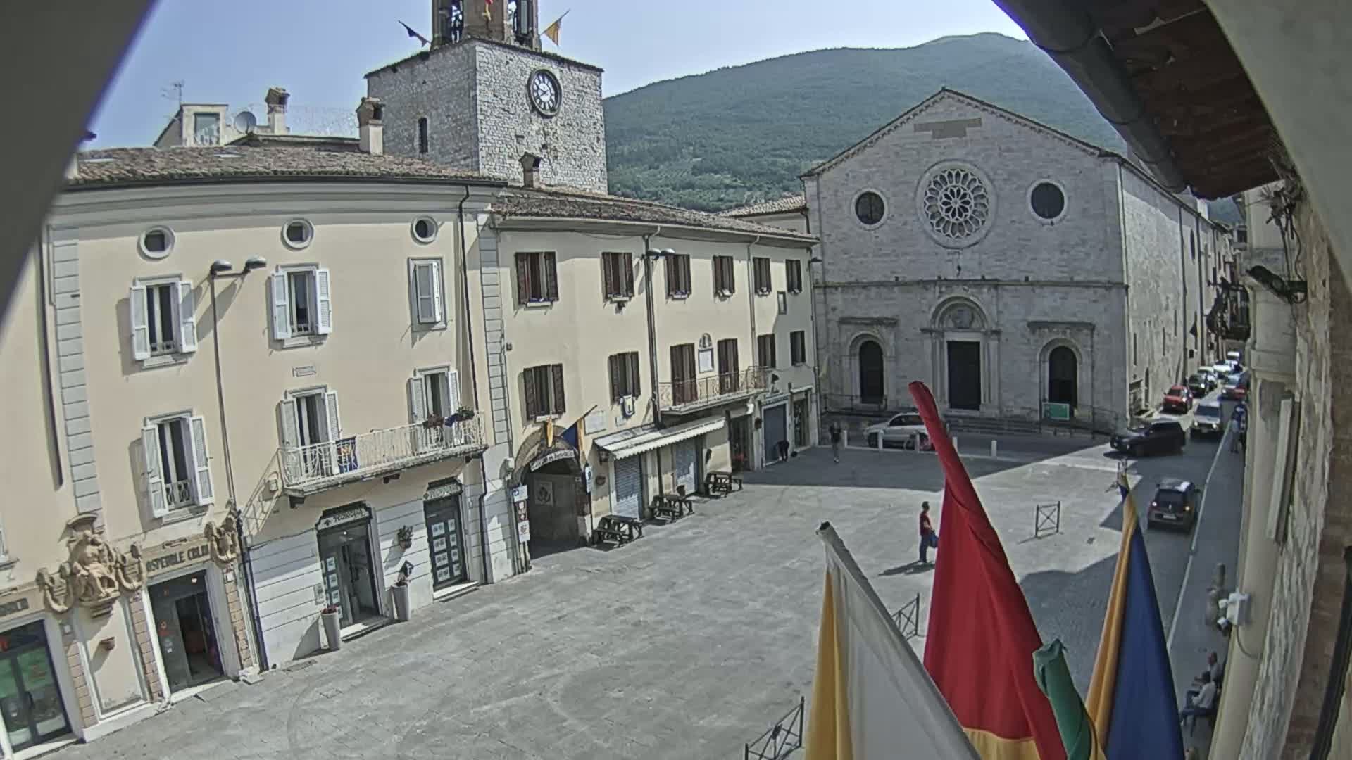 A town square with several buildings, including a church with a rose window and a clock tower, under a sunny sky.