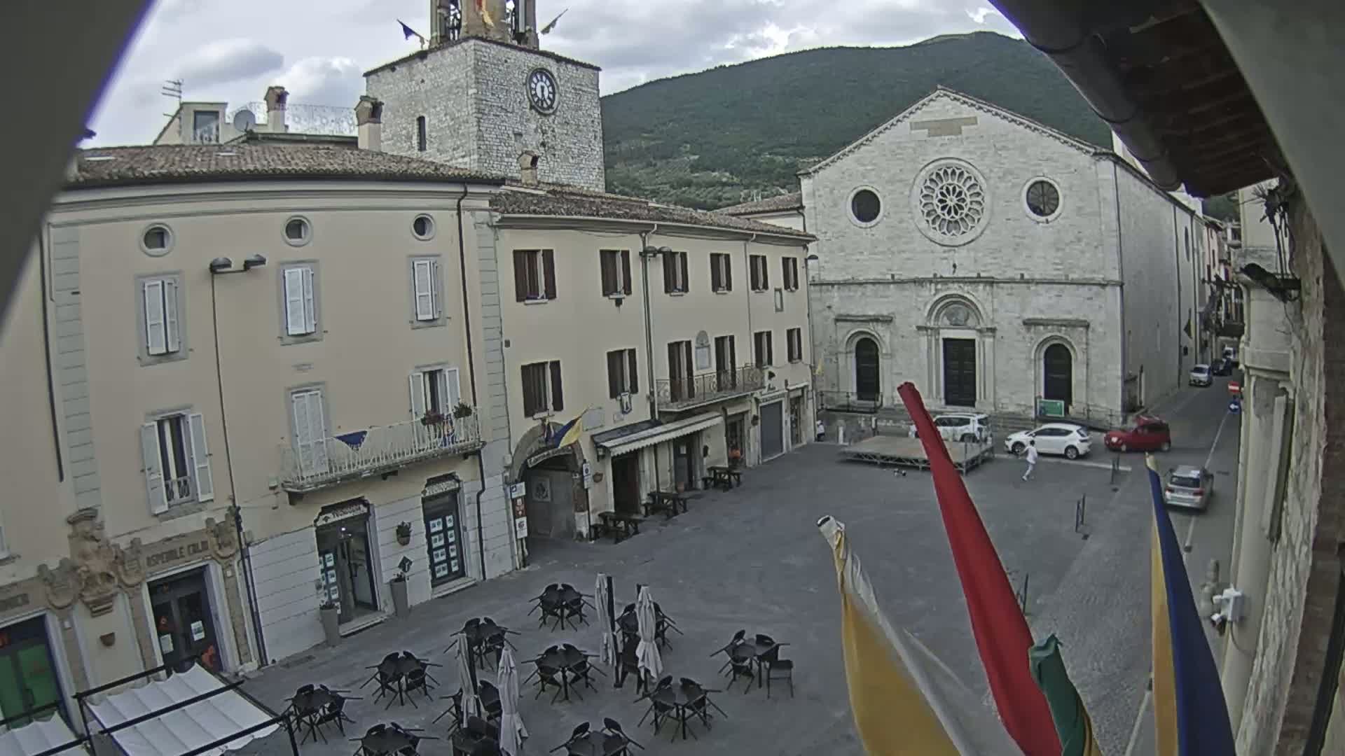 A town square with several buildings, including a church with a rose window and a clock tower, is mostly empty under an overcast sky.