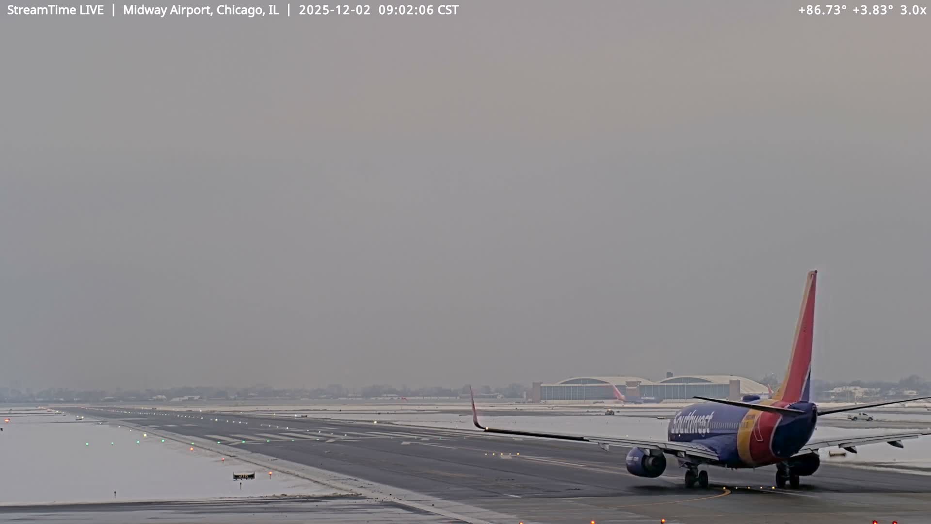 A Southwest Airlines plane is visible from the rear on a snow-lined airport runway under an overcast, gray sky.