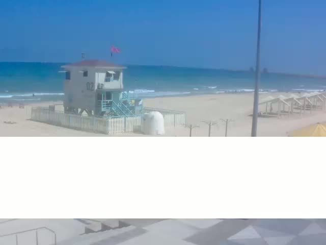 A lifeguard station stands on a sandy beach under a clear blue sky with a calm ocean in the background.