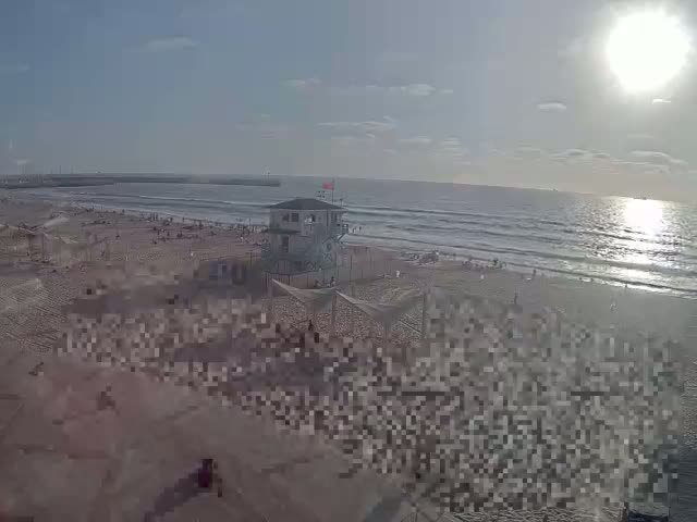 A sandy beach with a lifeguard station, several beach umbrellas, and a calm ocean under a clear blue sky.