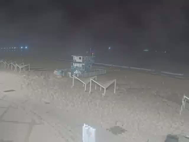 A mostly empty beach at night is shown with a lifeguard stand and several empty beach structures.