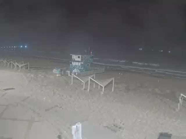 A mostly empty beach at night is shown with a lifeguard stand and several empty beach structures.