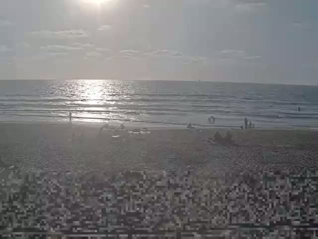 A wide sandy beach with small waves rolling onto the shore under a clear blue sky.