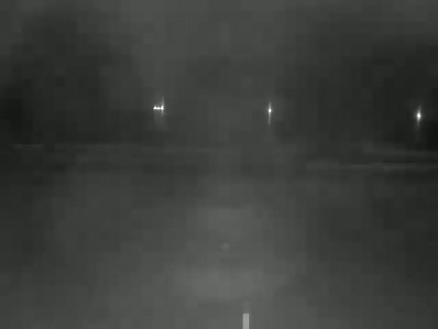 A dark, nighttime scene shows a road with faint lights in the distance and a blurry foreground.
