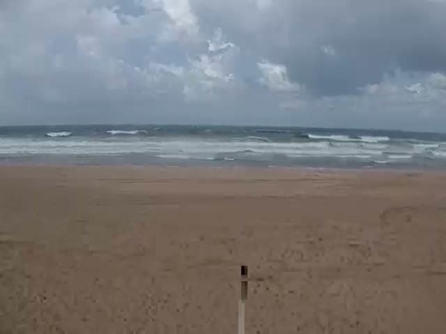 A sandy beach stretches towards a choppy ocean with white-capped waves under a heavily overcast sky.