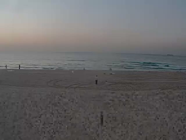 A sandy beach stretches towards a choppy ocean with white-capped waves under a heavily overcast sky.